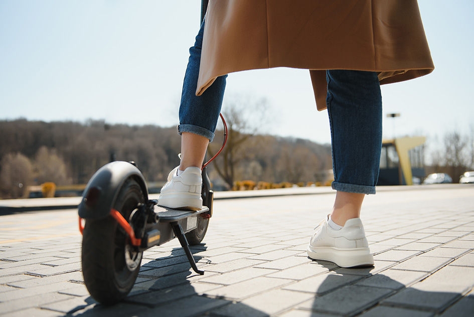 Close up of woman riding black electric kick scooter at cityscape, motion blur