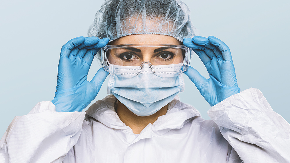 ziekenhuismedewerkster met mondkapje en haarnetje op zet een veiligheidsbril op