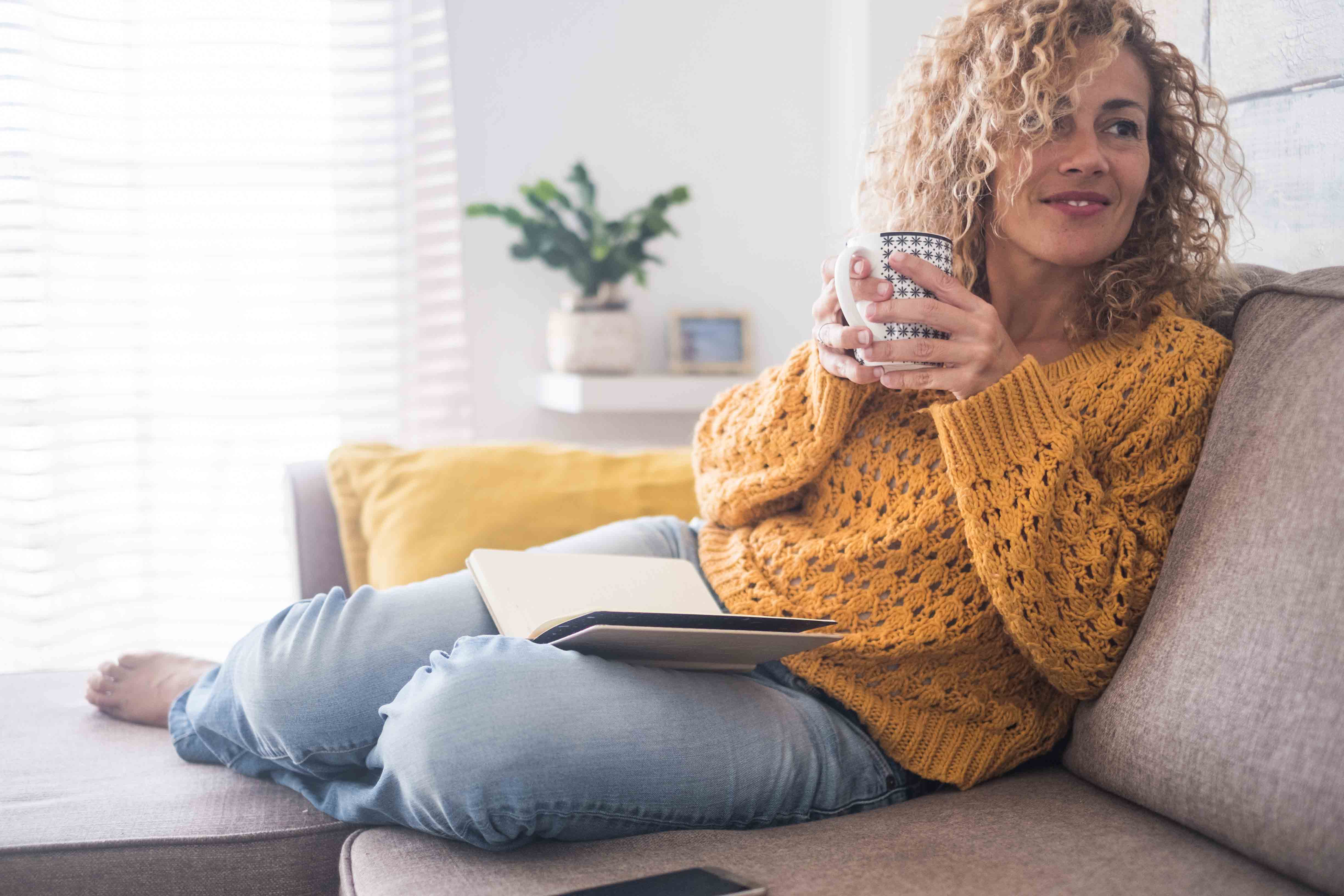 vrouw met ileostoma kijkt de woonkamer in vanaf haar bank met een kop warme drank